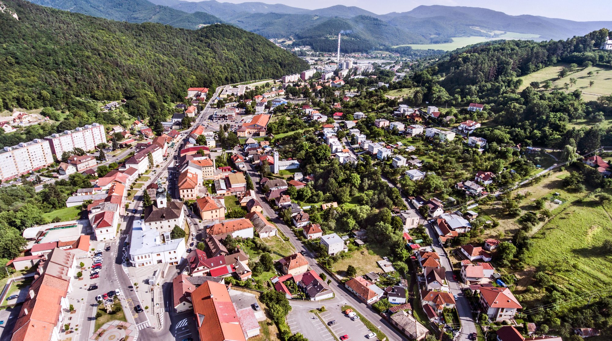 Letecký pohľad na menšie slovenské okresné mesto v údolí, sídlisko aj historické centrum, v pozadí zalesnené kopce